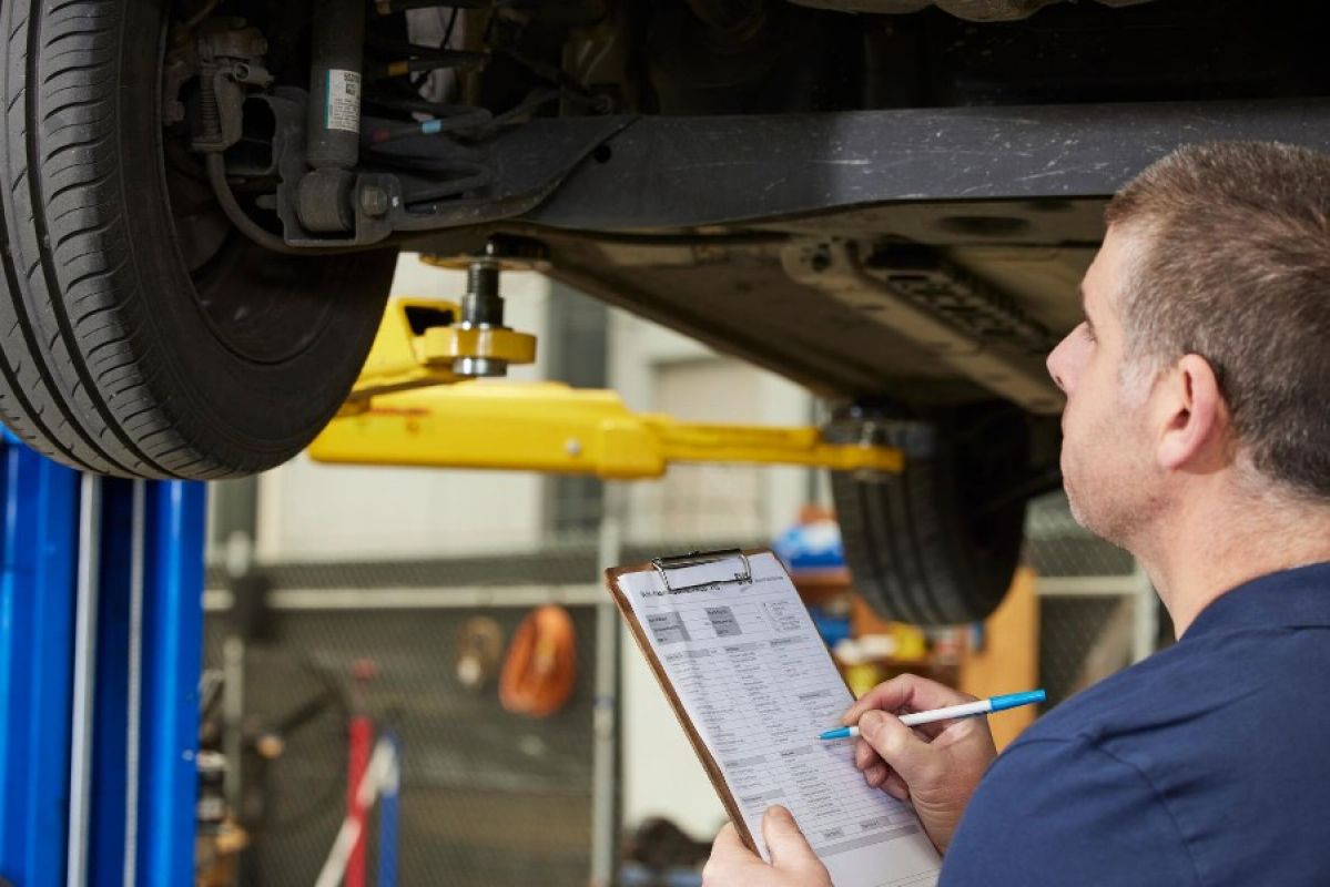 A mechanic examines underneath a car