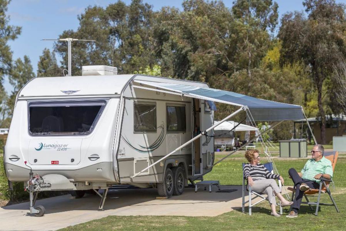 woman and man relaxing outside their parked caravan