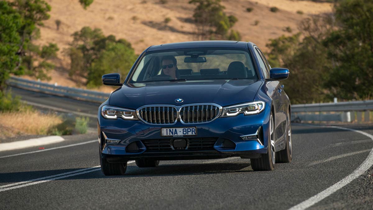 A blue BMW 330i M Sport sedan driving on a curved country road