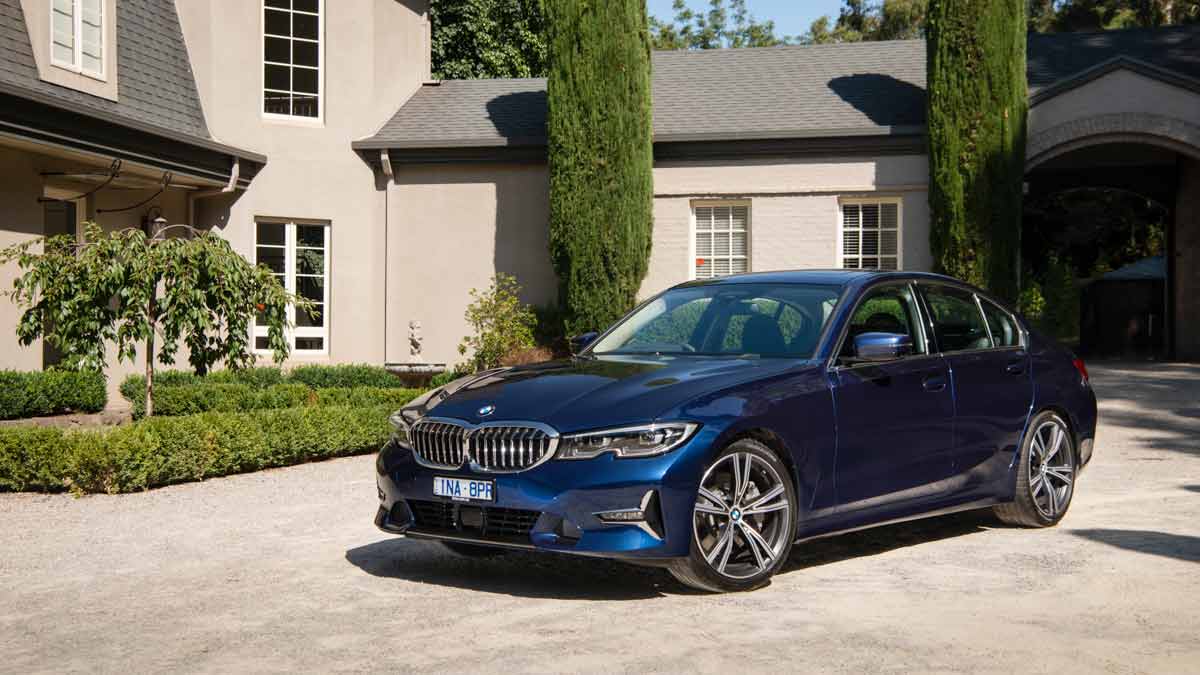 Front side view of a blue BMW 330i M Sport sedan parked at a country estate