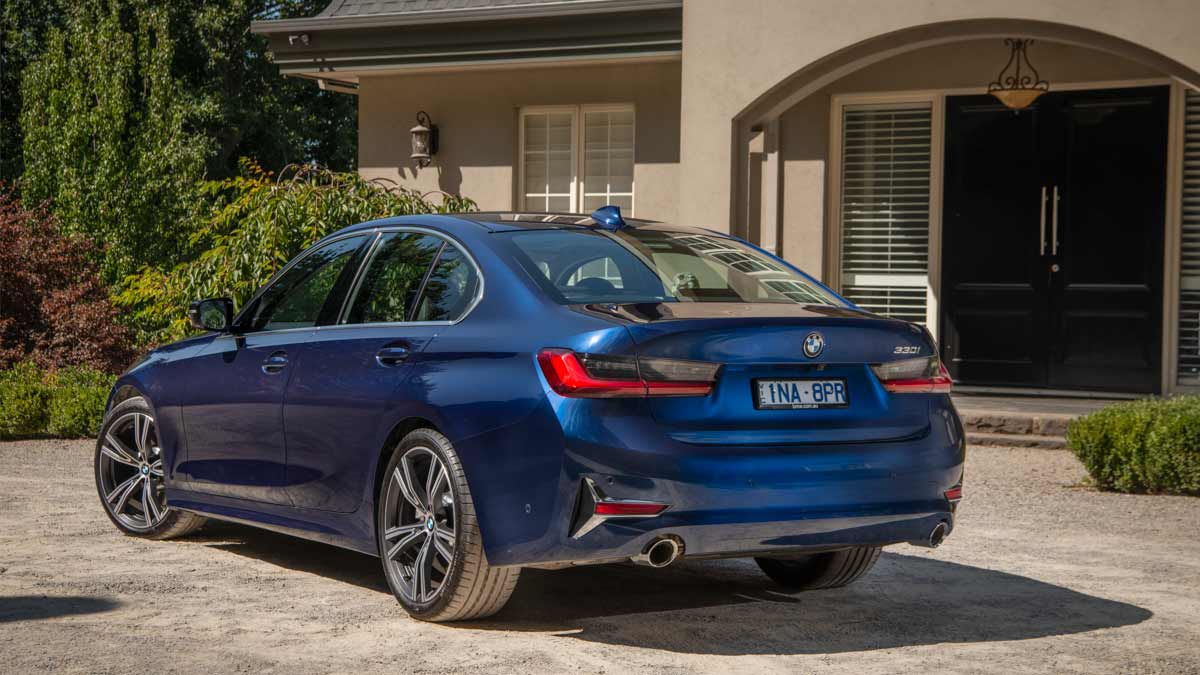 Rear side view of a blue BMW 330i M Sport sedan parked at a country estate