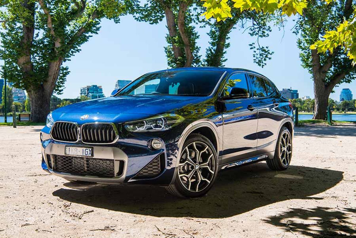 Blue BMW X2 sDrive 20i parked in front of a lake on a sunny day