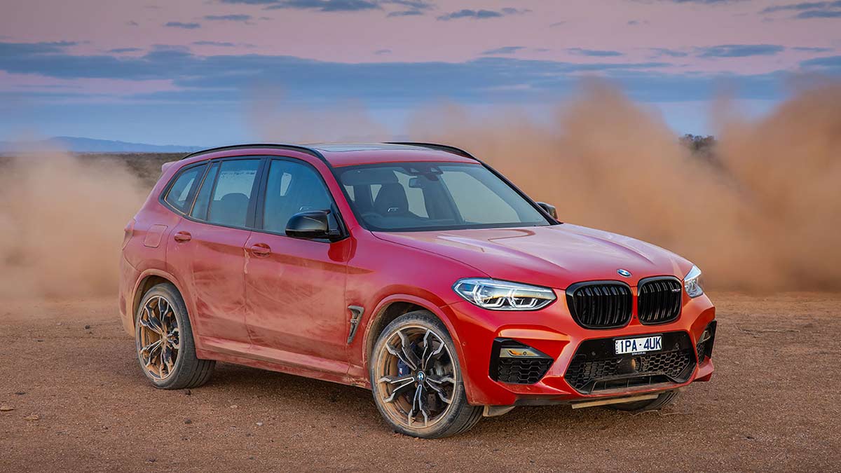 Front side view of a red BMW X3 M Competition 2020 car kicking up dust in a desert landscape