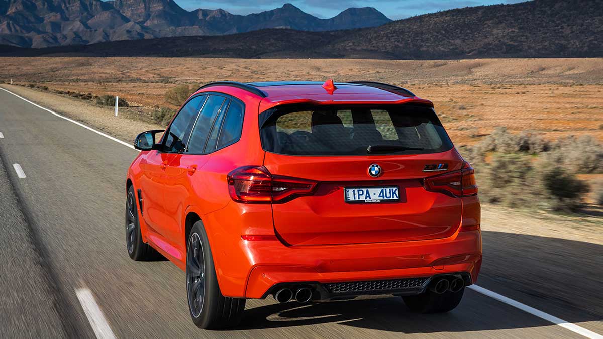 Rear side view of a red BMW X3 M Competition 2020 car driving down a straight road in the desert