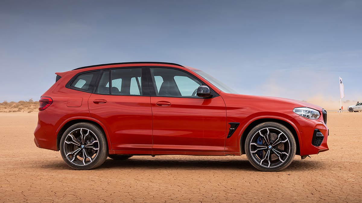 Side profile view of a red BMW X3 M Competition 2020 car in a desert landscape