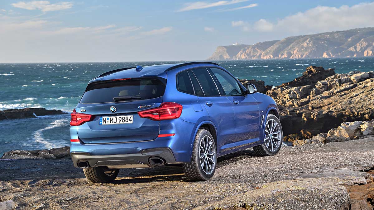 Rear side view of a blue BMW X3 parked on a beach