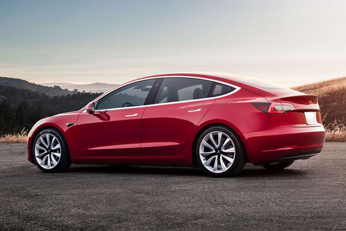 Side rear view of a parked red Tesla Model 3 car at sunset