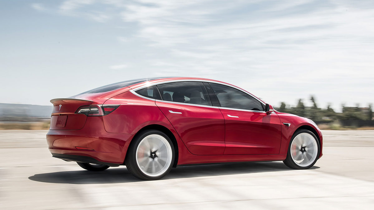 Side rear view of a red Tesla Model 3 in motion