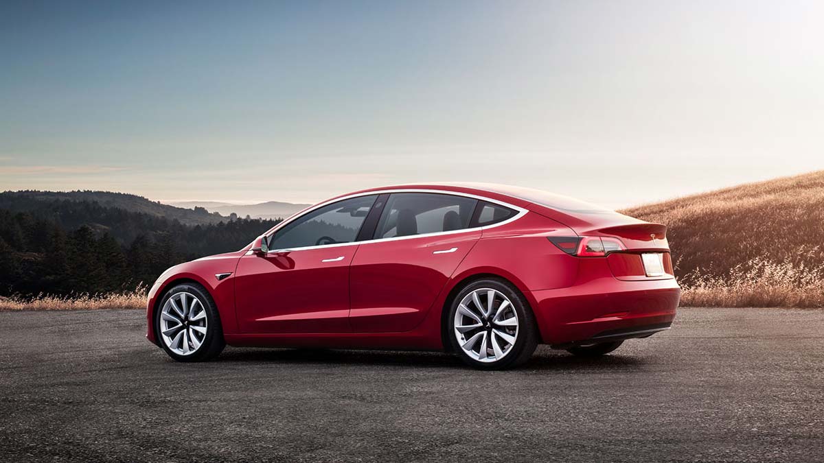 Side rear view of a parked red Tesla Model 3 car at sunset