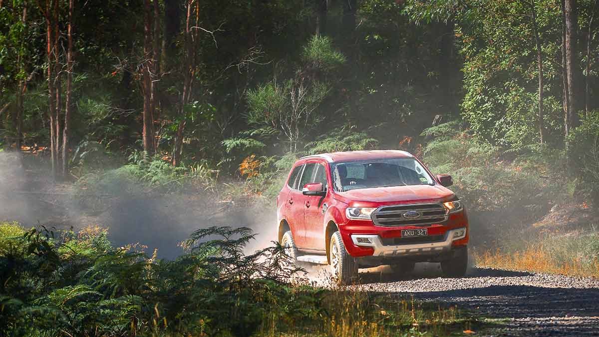 A red Ford Everest Trend driving on a dusty, dirt road