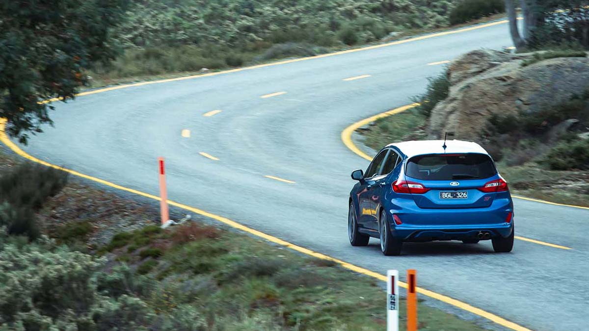 Rear side view of a blue Ford Fiesta ST 2020 car driving on a winding road