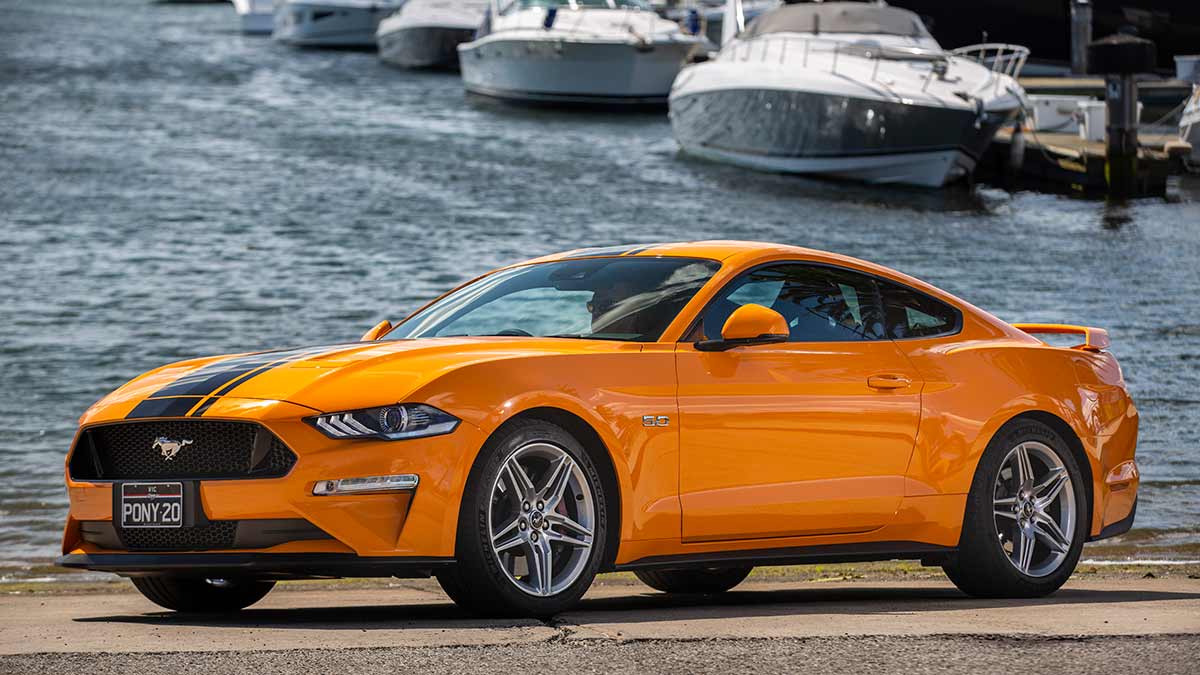 Front side view of an orange Ford Mustang parked by the water