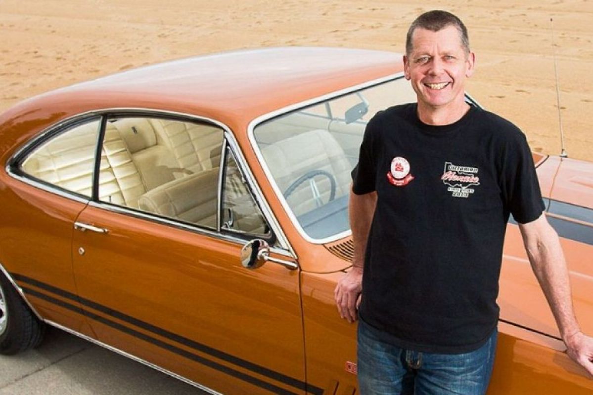 man standing in front of orange holden monaro