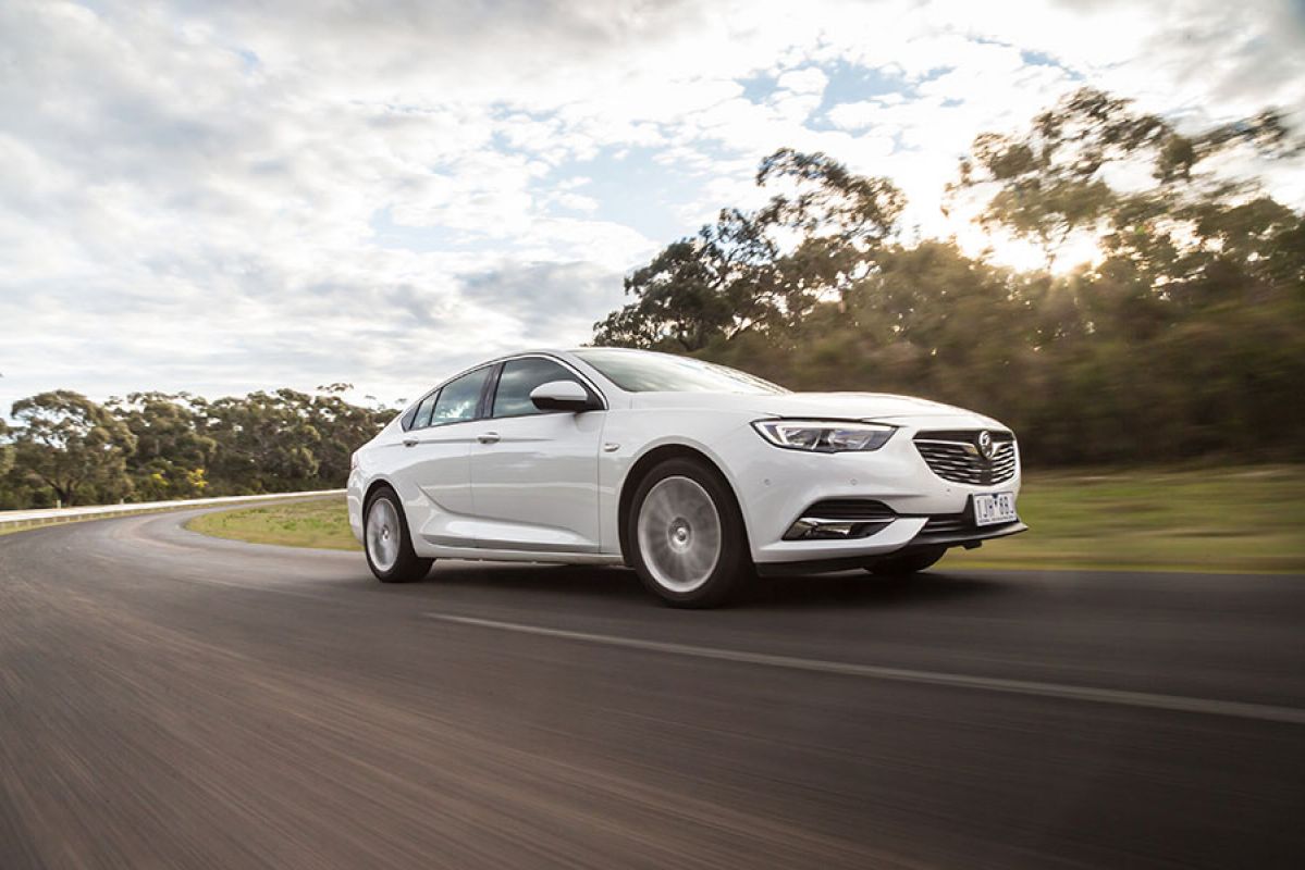 A white Holden ZB Commoedore driving on a curved road