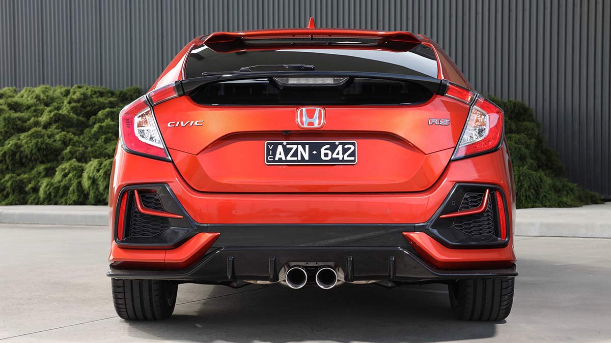 Rear view of a metallic orange-red Honda Civic RS hatch 2020 car parked on concrete in front of a dark grey corrugated wall