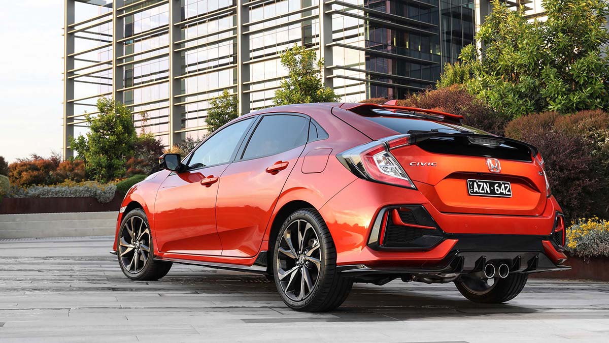 Rear  side view of a metallic orange-red Honda Civic RS hatch 2020 car parked on concrete in front of a building