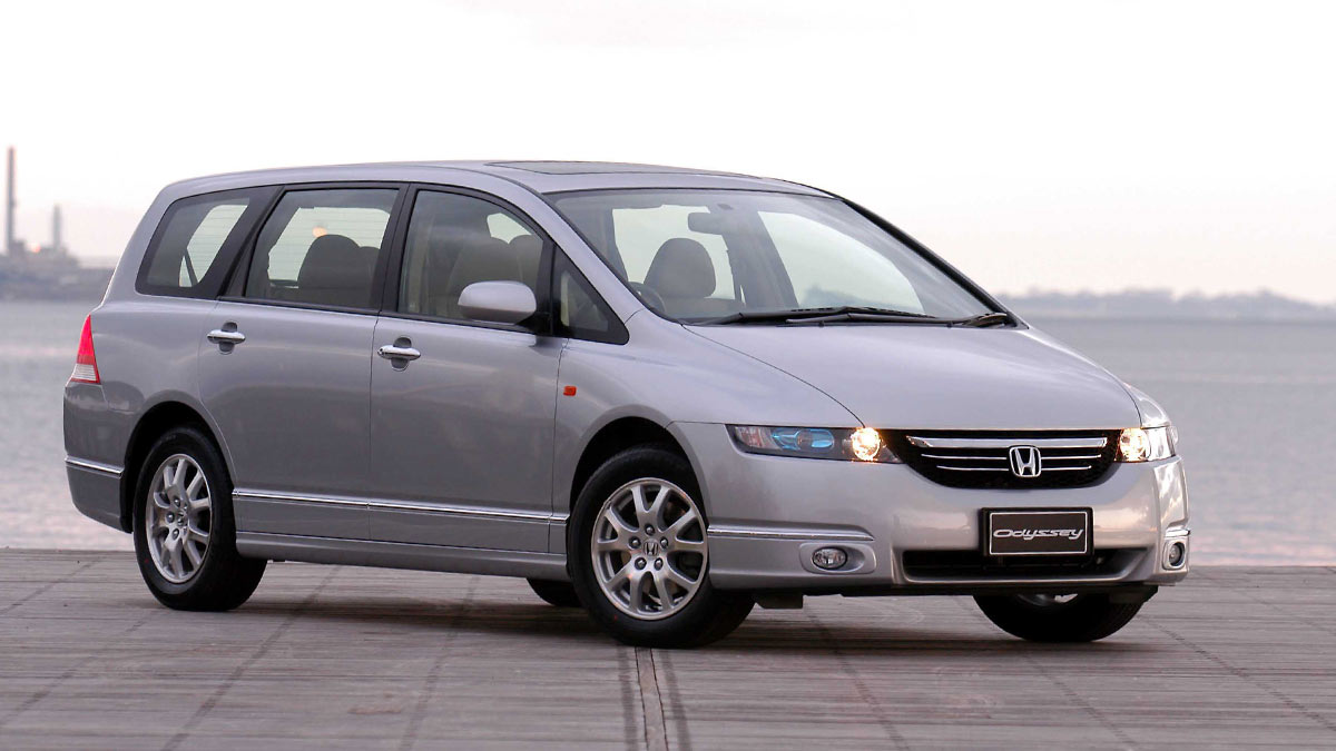 Front side view of a silver Honda Odyssey parked next to a body of water