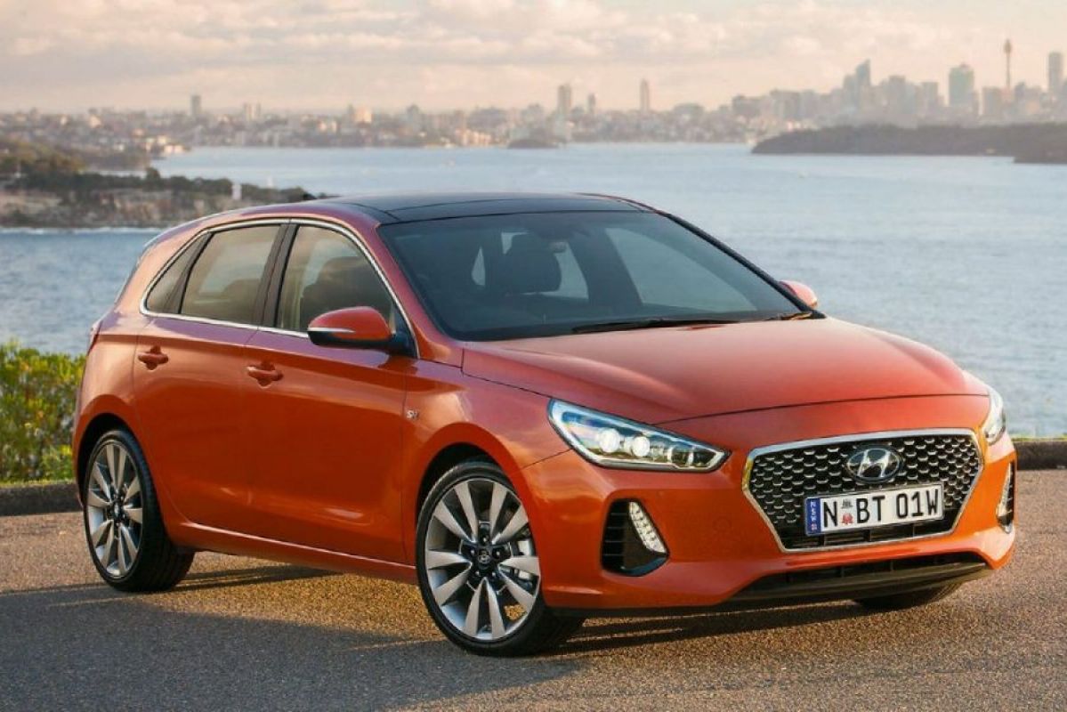 orange hyundai i30 parked on road next to river in front of city skyline