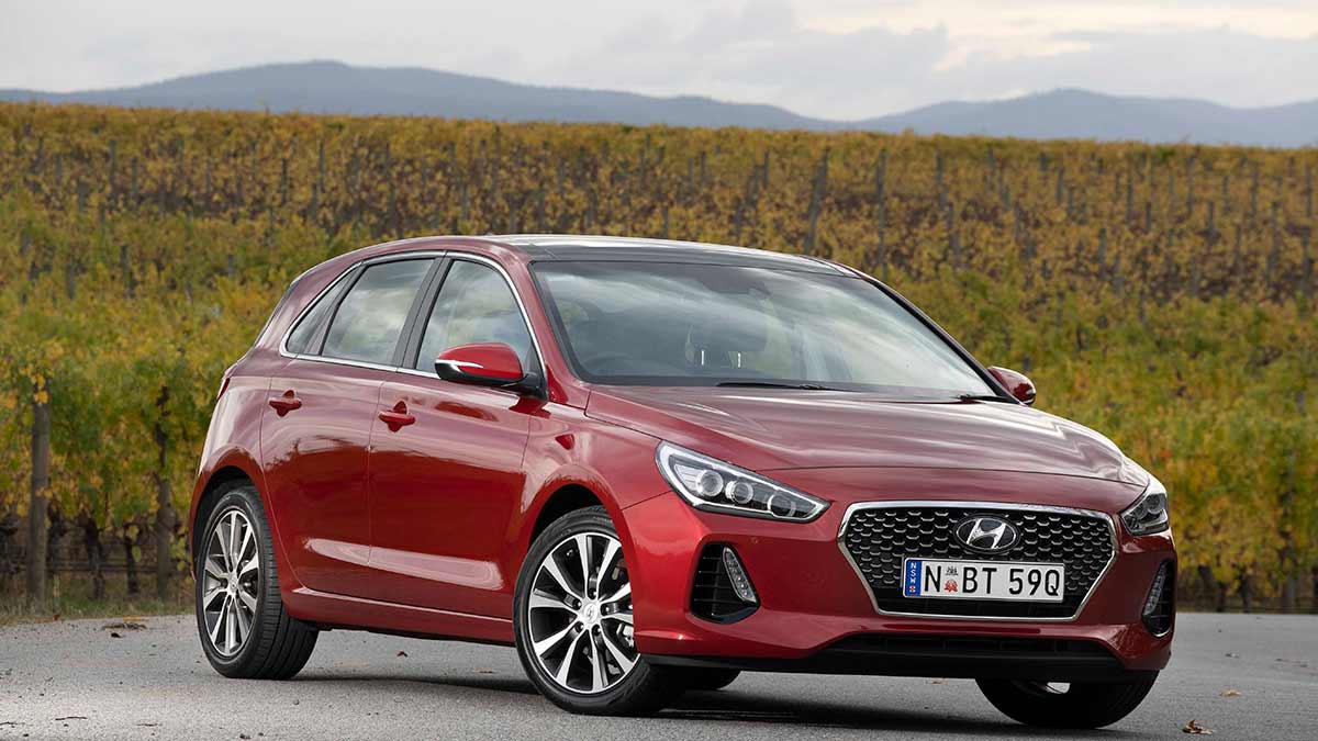 Front side view of a red Hyundai i30 parked on a highway in the countryside