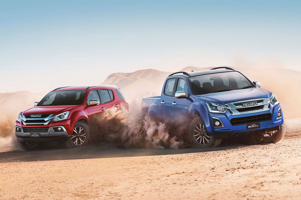 A red Isuzu MU-X next to a blue D-Max surrounded by dust clouds in a desert landscape