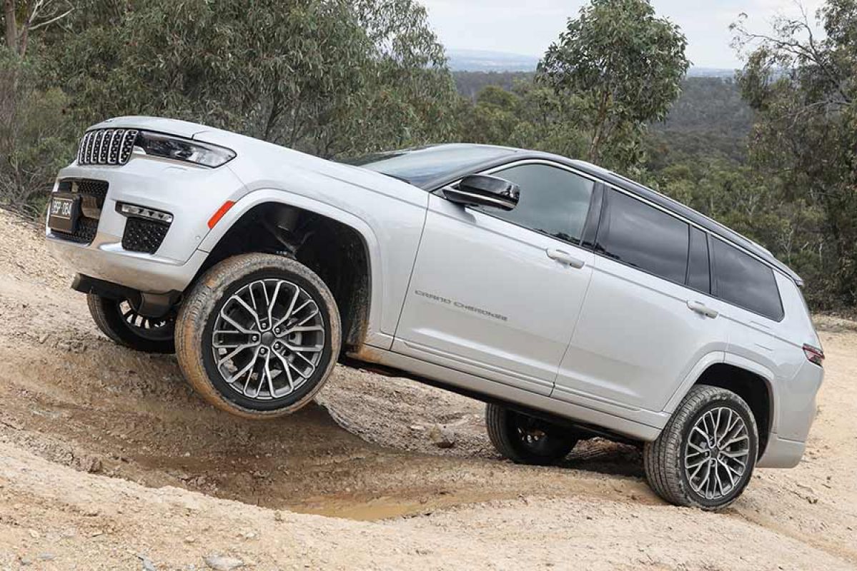 A silver Jeep Grand Cherokee L lifts a wheel driving off-road.