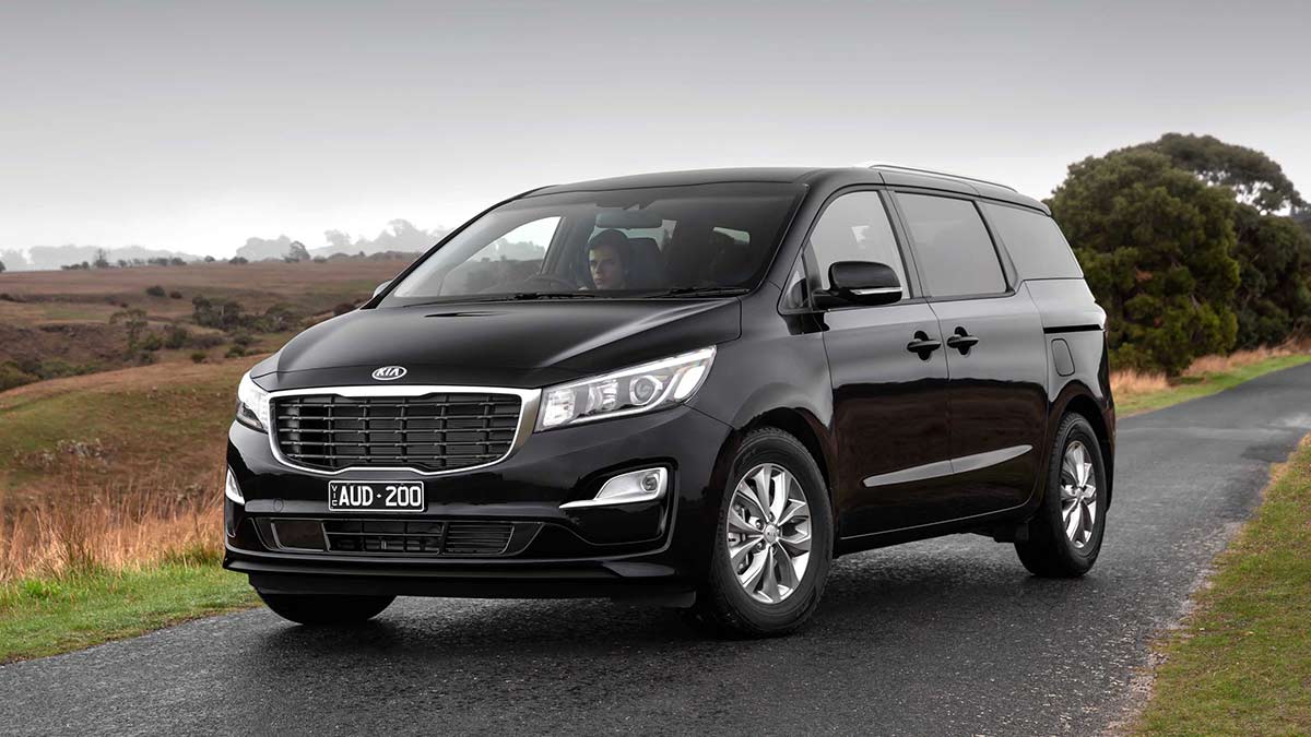 Front side view of a black Kia Carnival parked on a country road