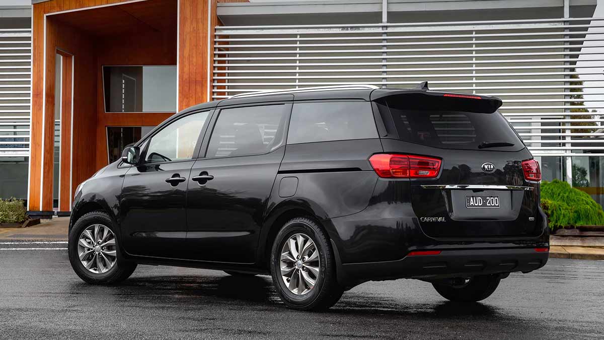 Rear side view of a black Kia Carnival parked in front of a building