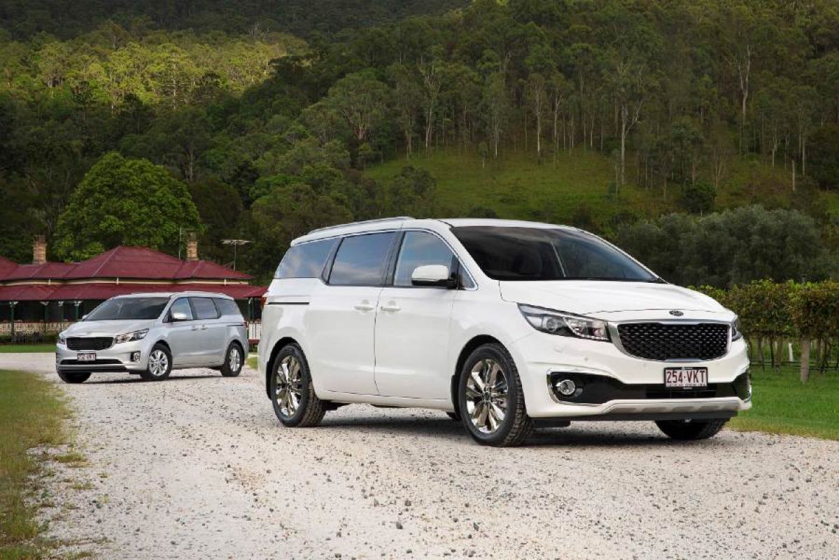 white kia carnival sli parked on dirt road in front of trees