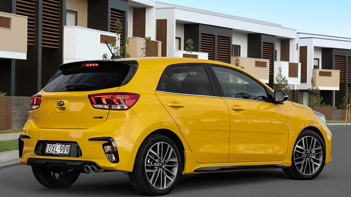 Rear side view of a yellow Kia Rio GT-Line parked in front of apartments