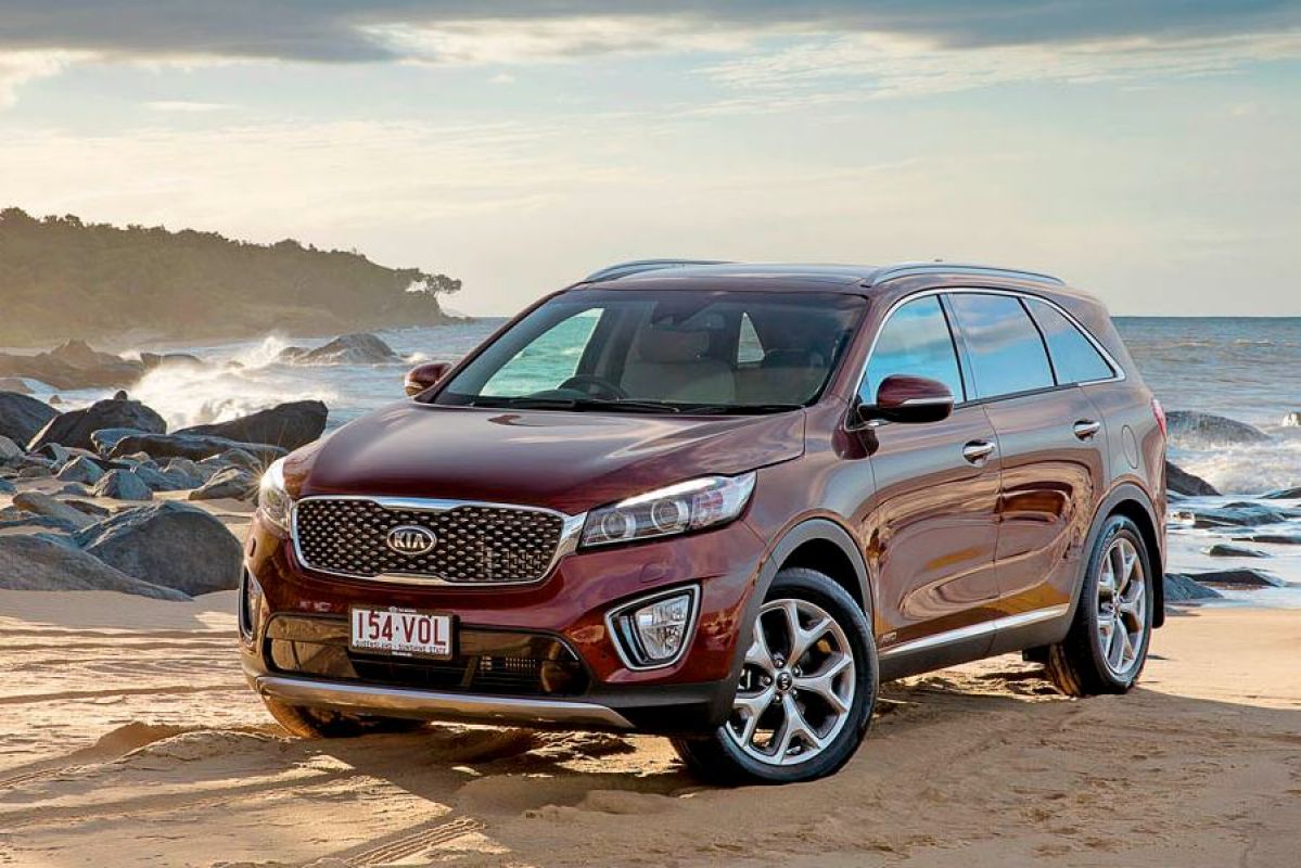 burnt orange kia sorento gt parked on beach next to rocks and waves