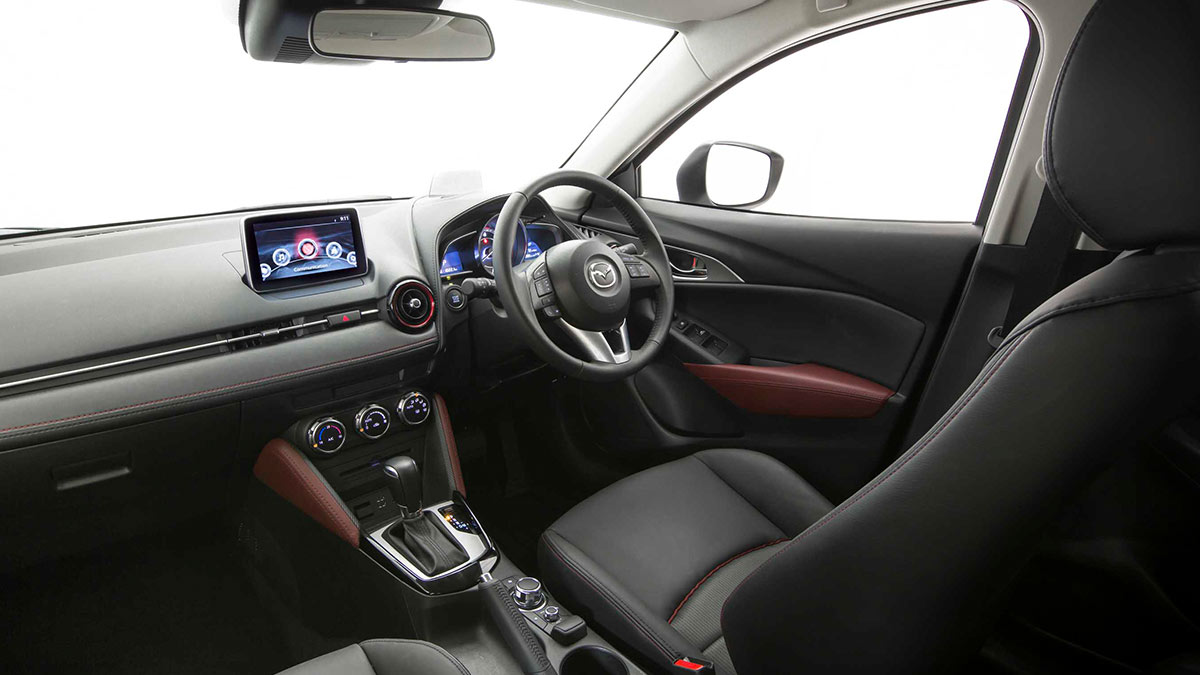 Black interior with red detailing of the Mazda CX-3 showing the driver's seat, centre console and steering wheel