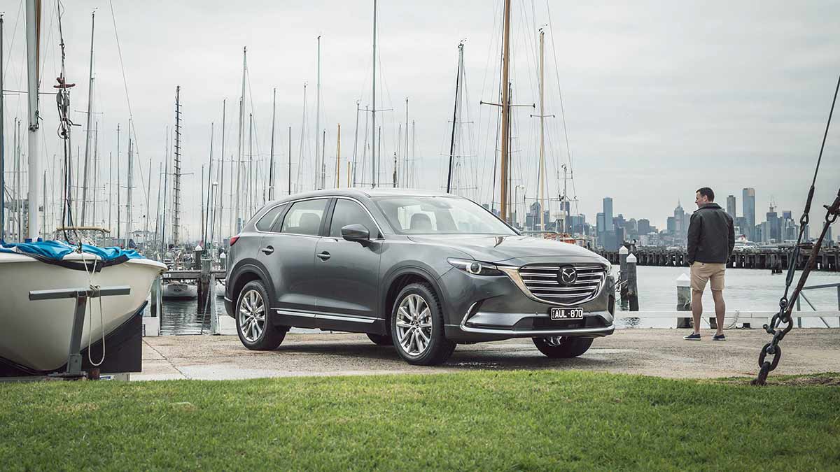 Front side view of a metallic grey Mazda CX-9 parked at a marina