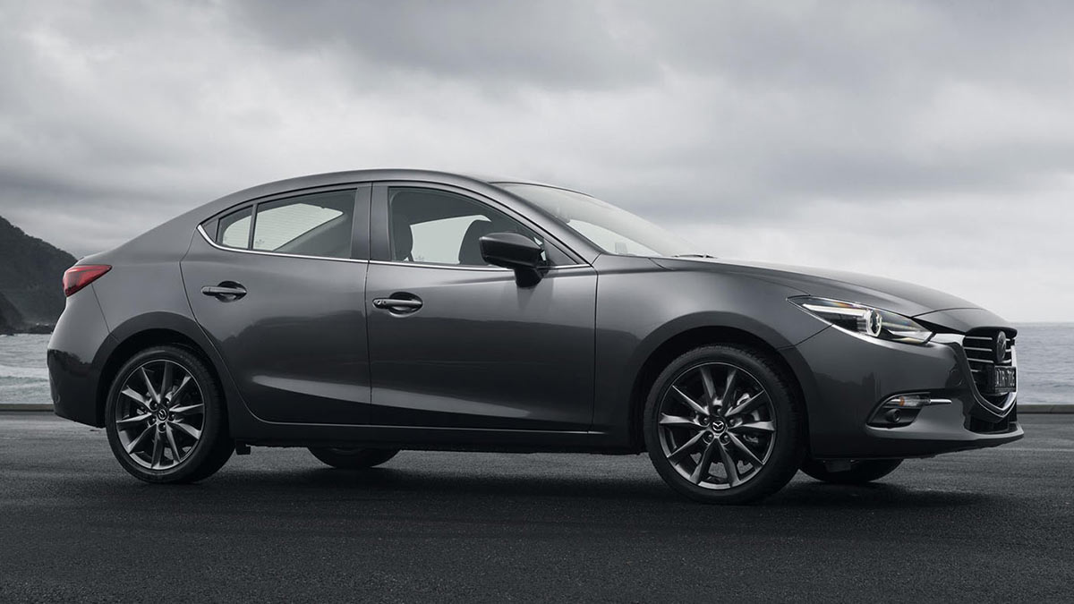 Side view of a dark grey Mazda3 parked on tarmac next to the sea