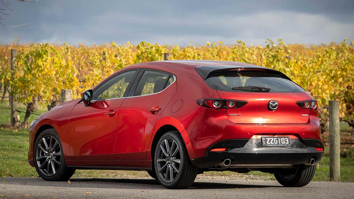 Rear side view of a red Mazda 3 G20 Elite parked on a highway in the countryside