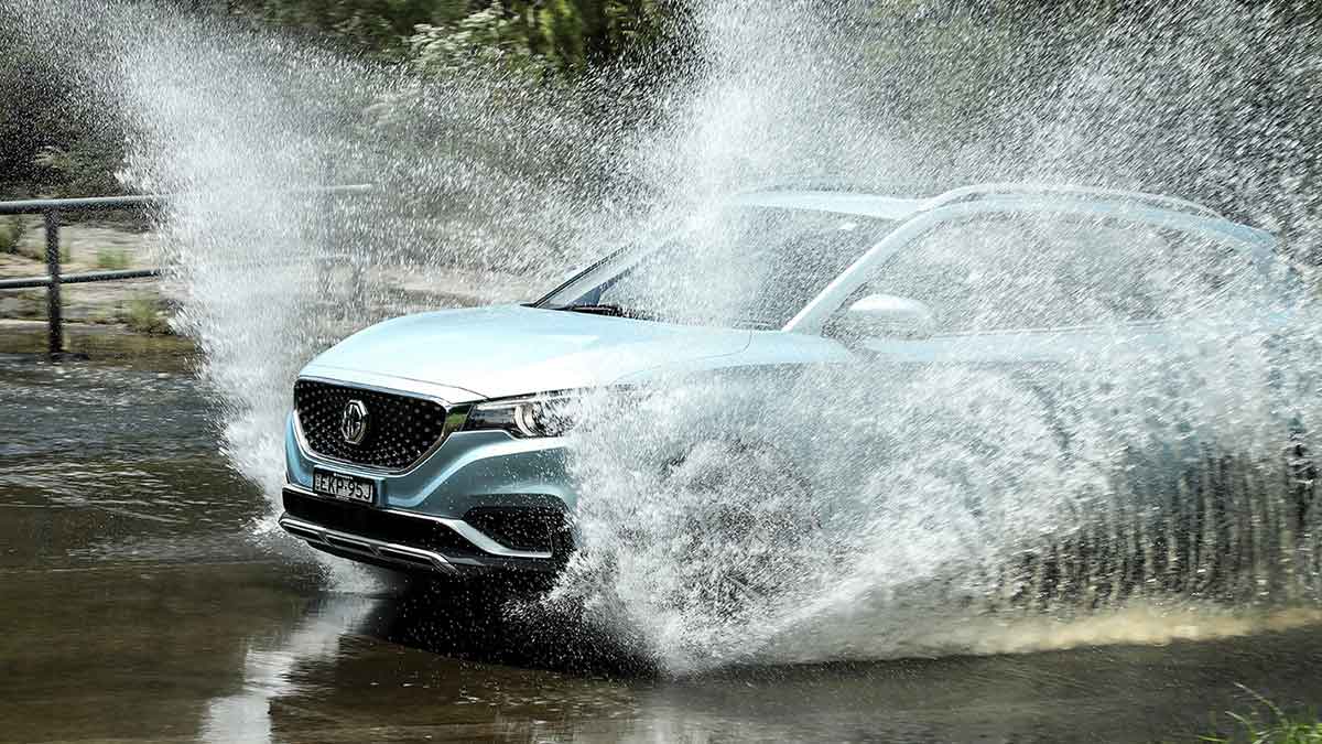 Light blue MG ZS electric vehicle driving through water with water spraying up