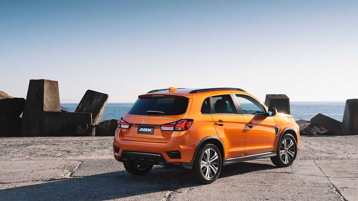 Rear side view of an orange Mitsubishi ASX parked on a cliff facing the ocean