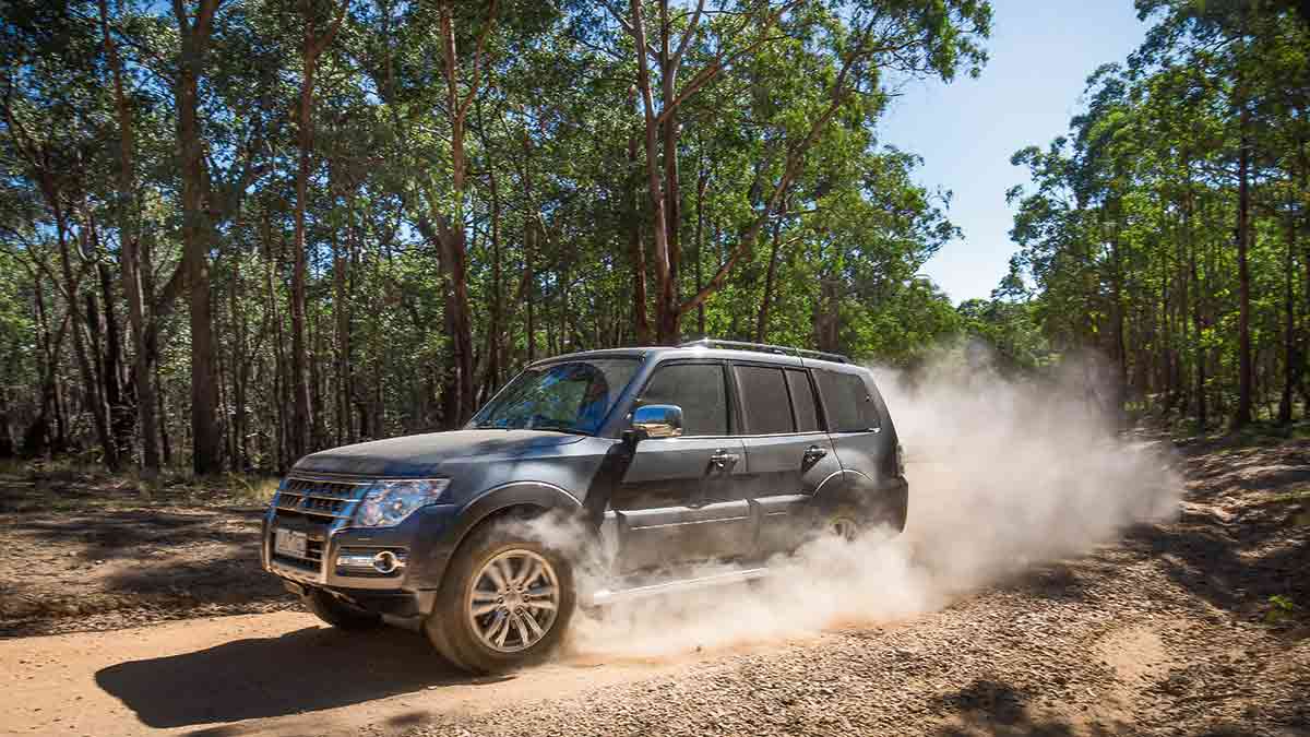 A grey Mitsubishi Pajero driving on a dusty, dirt road