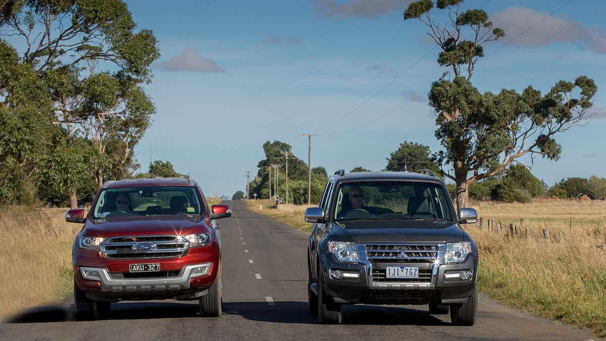 Front facing view of a red Ford Everest Trend driving next to a grey Mitsubishi Pajero on a country road