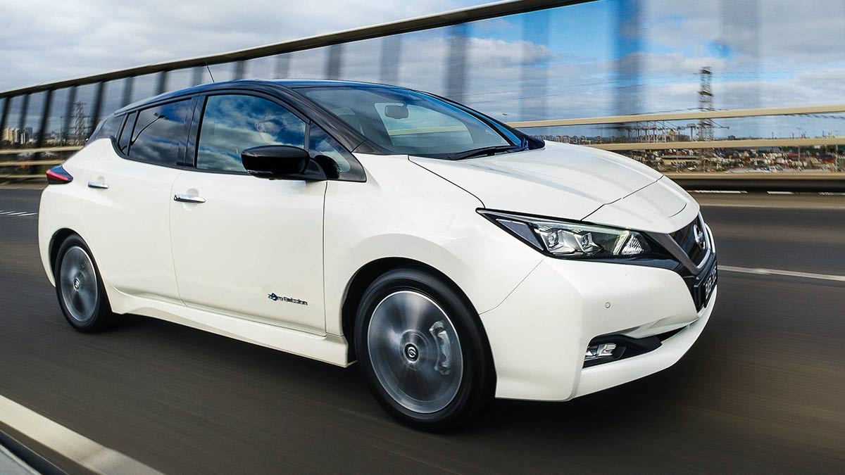 Front side view of a white Nissan Leaf in motion on a freeway