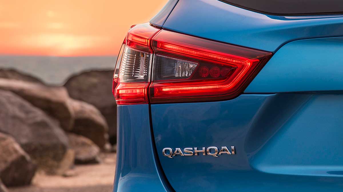 A blue Nissan Qashqai's taillight and Qashqai's logo at sunset