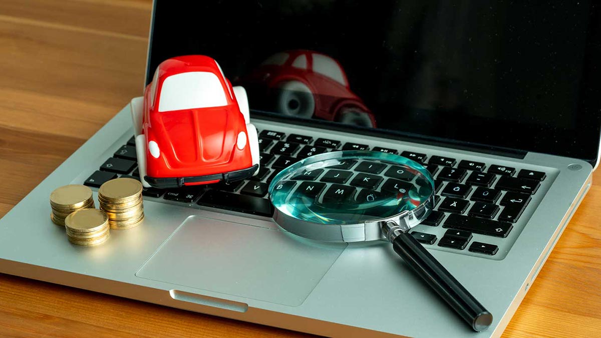 Laptop with toy car, coins and magnifying glass on top