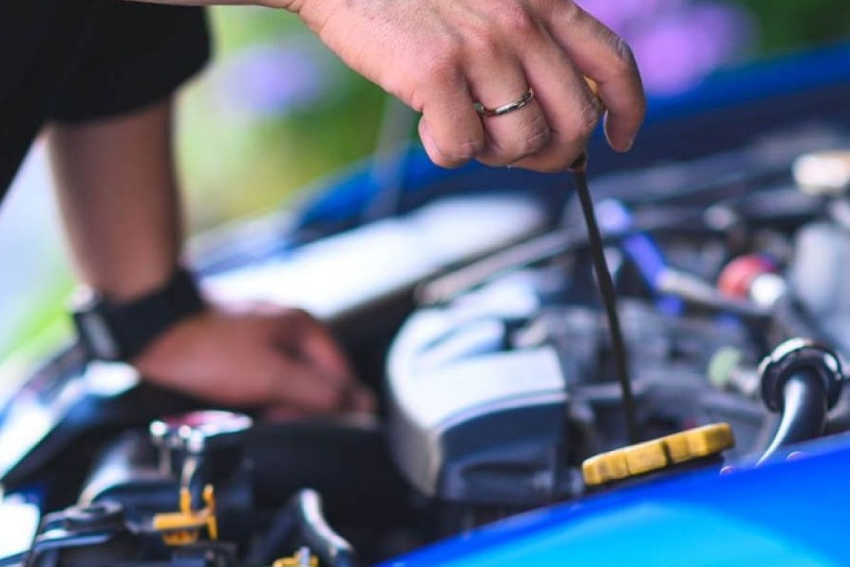 person changing oil in the hood of a blue car