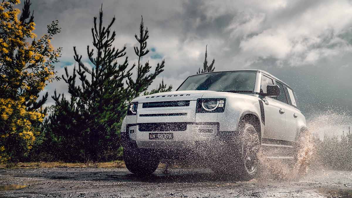 A silver Land Rover Defender being driven off-road through water