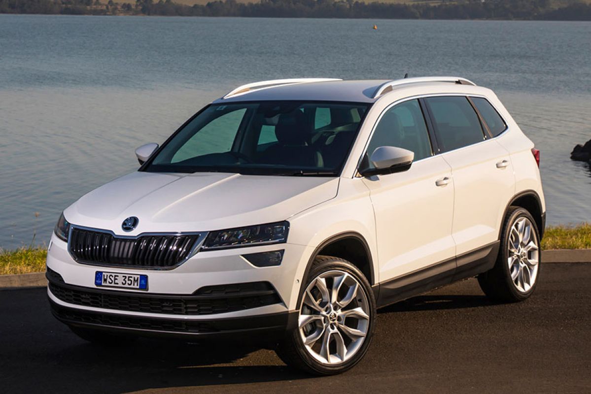 Front side view of a white Skoda Karoq 2019 car parked next to a lake