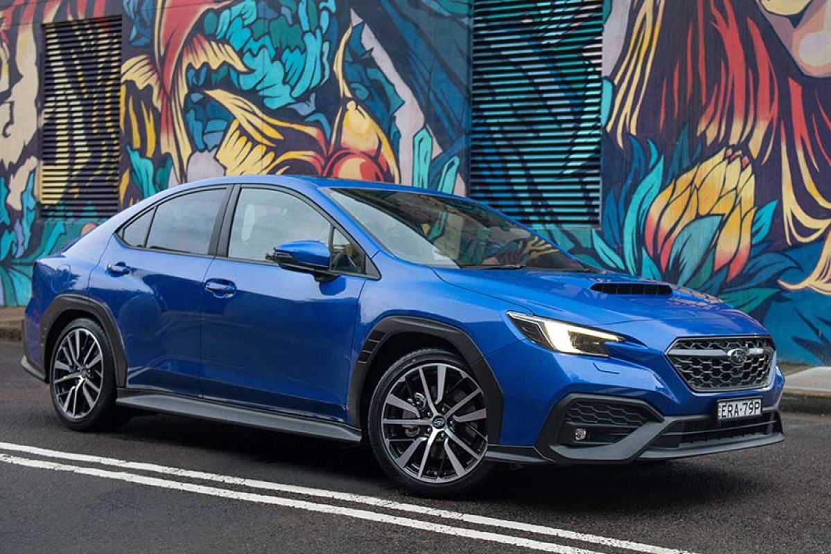 A blue Subaru WRX sedan is parked outside street art.