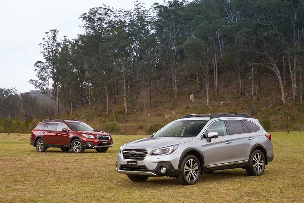 A red Subaru Outback parked near a grey Subaru Outback at alternating angles in the woods