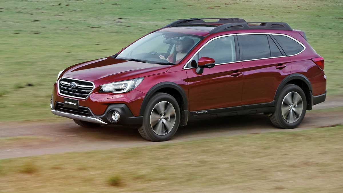 A red Subaru Outback driving on a dirt road