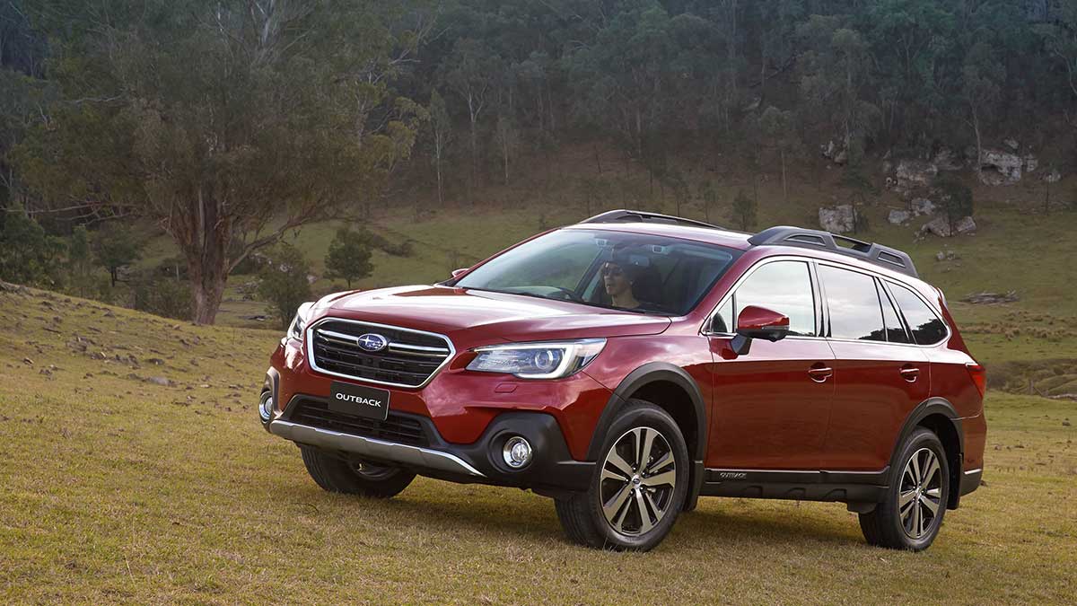 A red Subaru Outback driving up a grassy hill