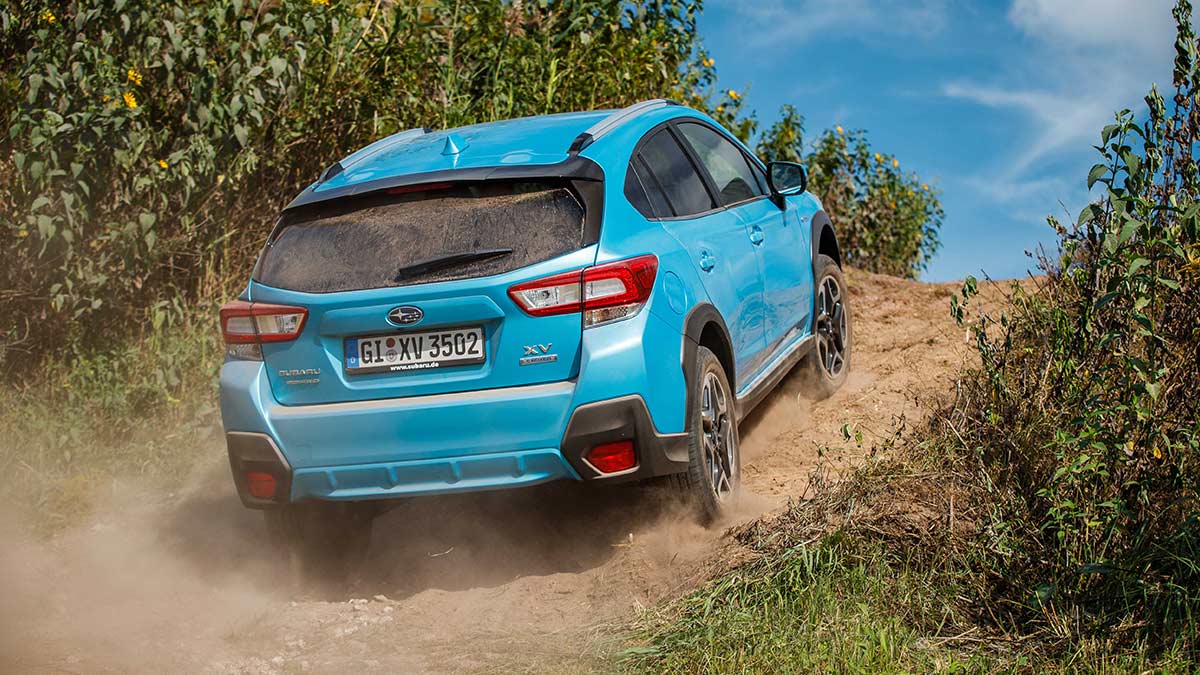 Rear side view of a light blue Subaru XV Hybrid 2020 car scaling an inclined dirt road