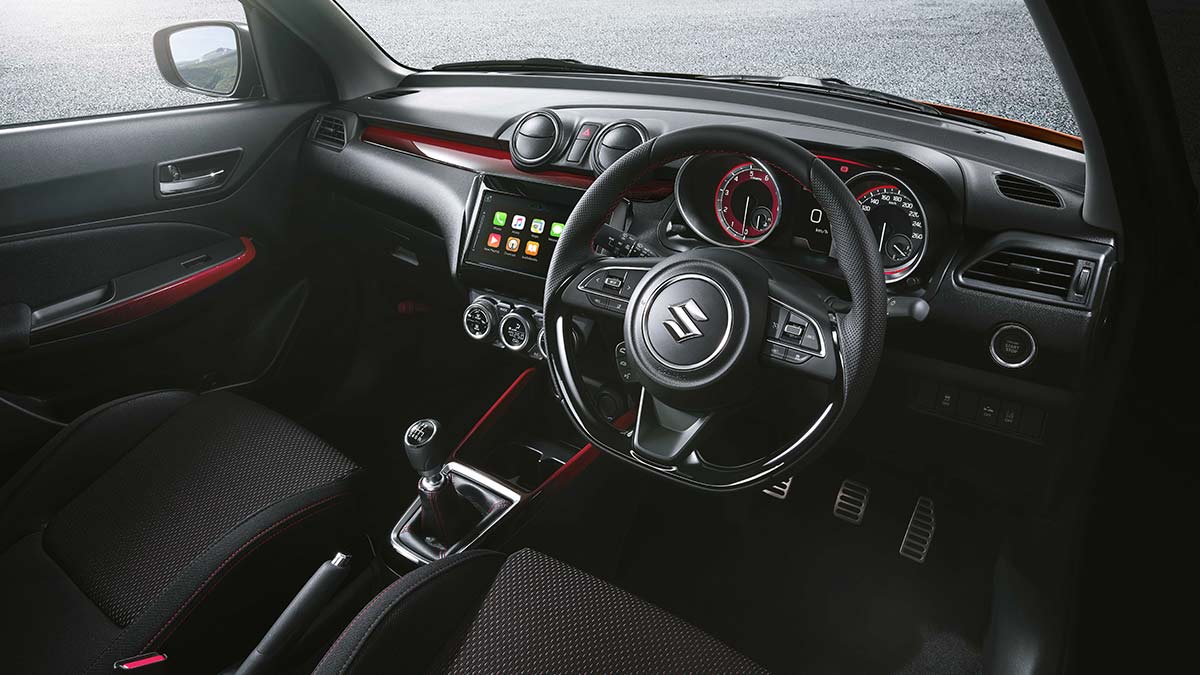 Dark grey interior with red detailing of the Suzuki Swift Sport 2020 showing the dashboard, centre console and steering wheel